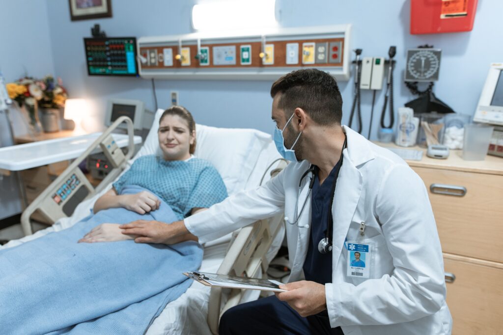 Doctor in a mask and white coat comforting a patient in a hospital bed, with a stethoscope and clipboard, illustrating when critical illness insurance helps