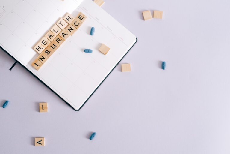 Wooden tiles spelling health insurance beside blue pills and a planner, representing the HSA vs. FSA decision for self-employed individuals