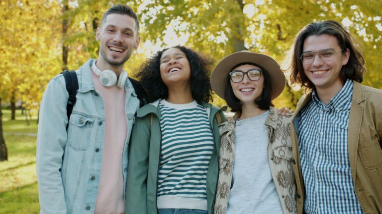 Diverse group of four young adults smiling together in a park with vibrant autumn leaves during open enrollment season