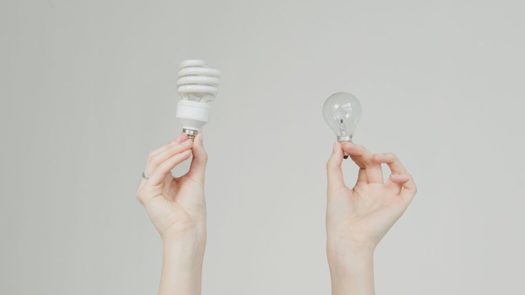 Hands comparing an incandescent bulb and an energy-efficient spiral bulb, like weighing a bronze plan supplemental insurance strategy against buying up.