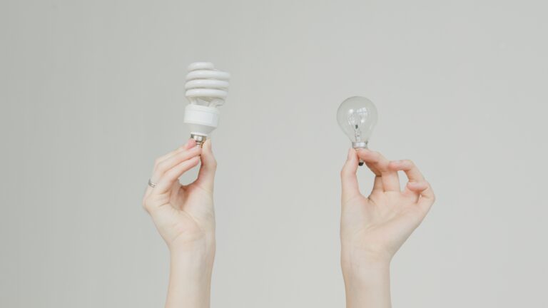 Hands comparing an incandescent bulb and an energy-efficient spiral bulb, like weighing a bronze plan supplemental insurance strategy against buying up.