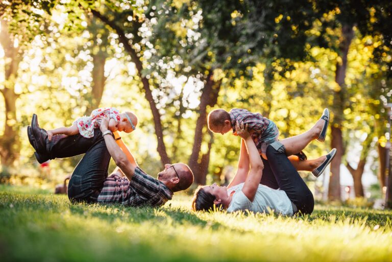 Parents and their young children playing together on the grass in a sunlit park, a picture of why life insurance matters to families.