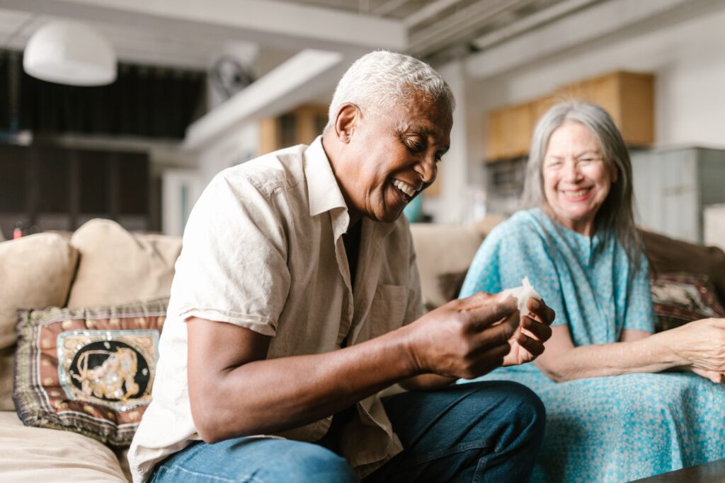 An older couple sitting close together on a sofa, laughing, relaxed about their Medicare coverage.