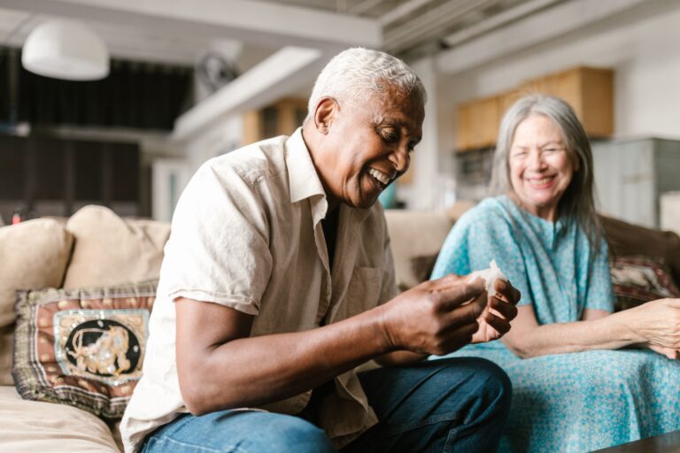 An older couple sitting close together on a sofa, laughing, relaxed about their Medicare coverage.